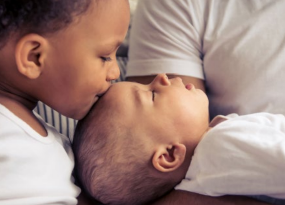 toddler kissing newborn on forehead