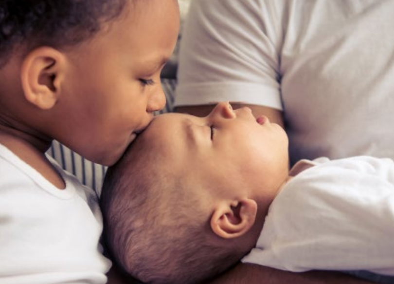 toddler kissing newborn on forehead