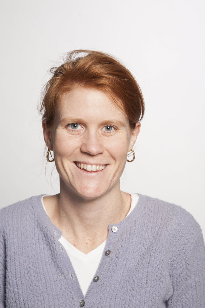 woman with red hair, earrings, and cardigan smiling at camera