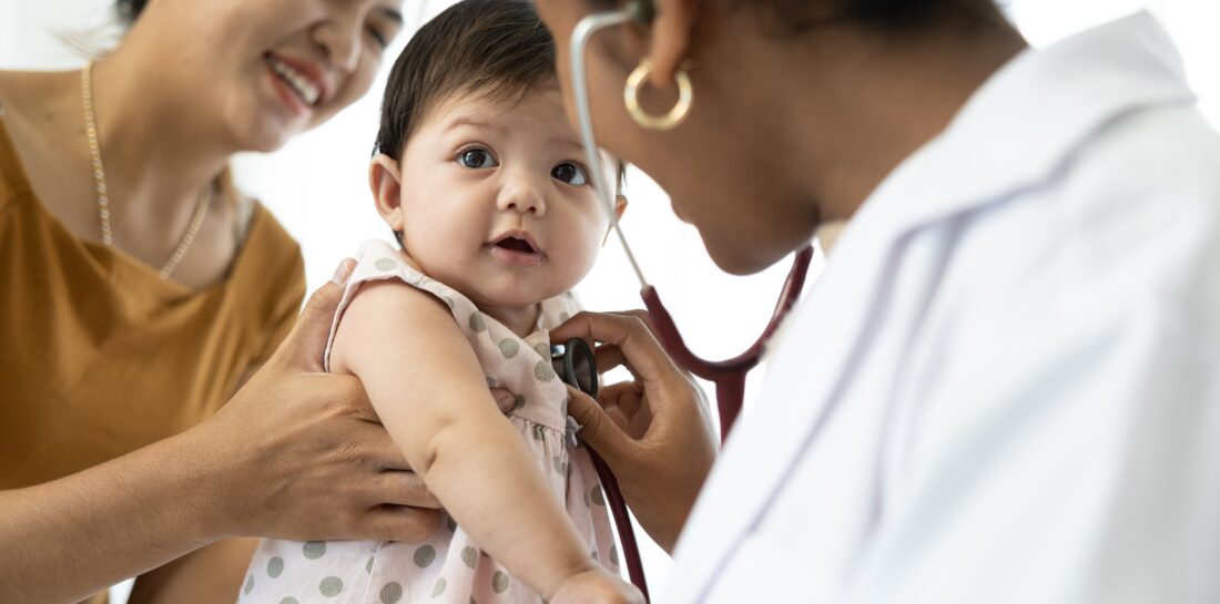 female health care provider holding stethoscope to toddler's chest, who is being held by a woman