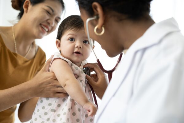 female health care provider holding stethoscope to toddler's chest, who is being held by a woman