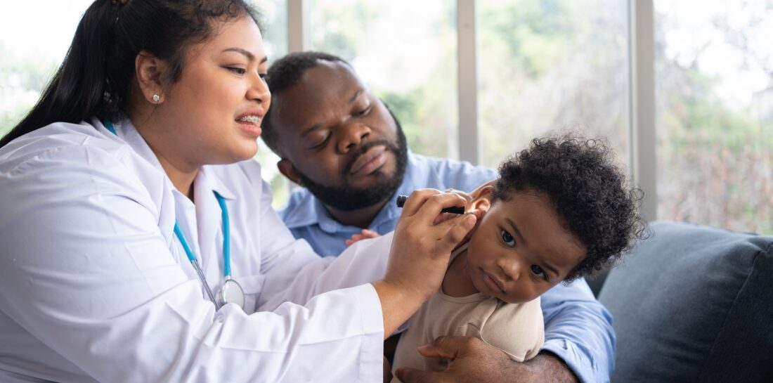 health care professional checking ears of toddler being held by dad
