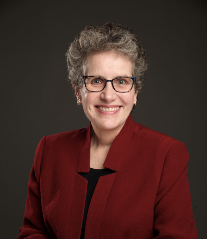 woman with glasses and red blazer smiler at camera