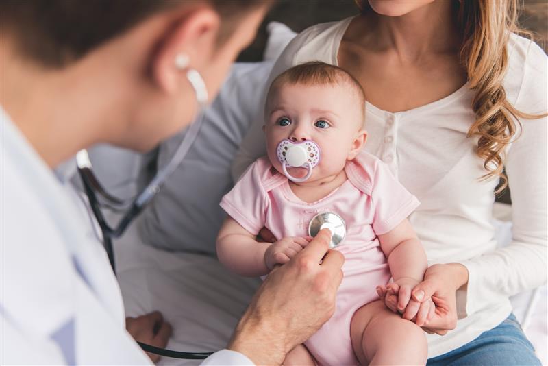 baby staring up at a doctor holding a stethoscope