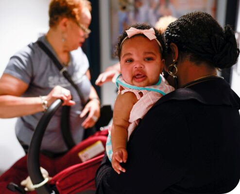 woman holding a baby with a woman in the background holding a carseat