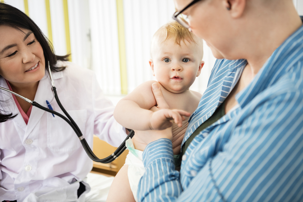 adult holding a baby while a medical professional uses a stethoscope