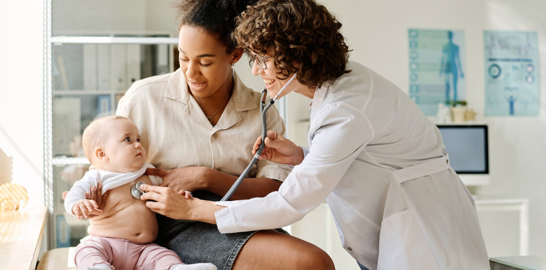 Doctor listening to child with stethoscope while sitting on hospital bed with mother