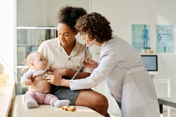 Doctor listening to child with stethoscope while sitting on hospital bed with mother