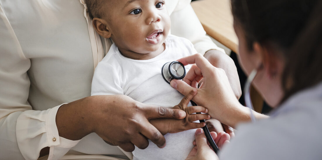 Medical professional holding stethoscope to smiling baby boy