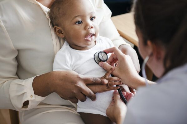 Medical professional holding stethoscope to smiling baby boy